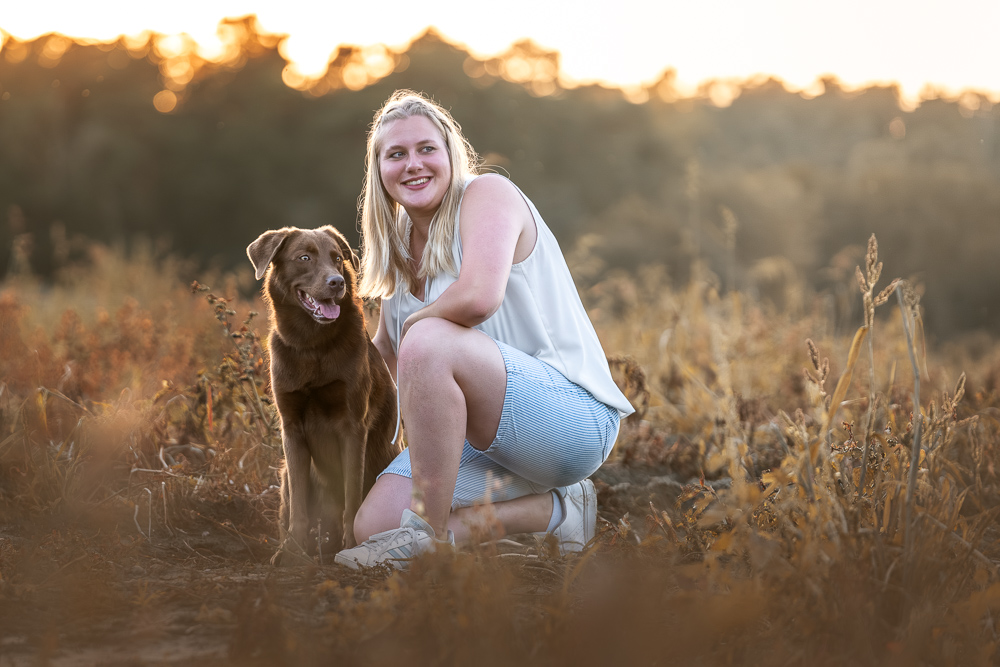 Foto von Lisa Werner Fotografie, Hund und Mensch, Frau sitzt neben einem Labrador im Sonnenuntergang