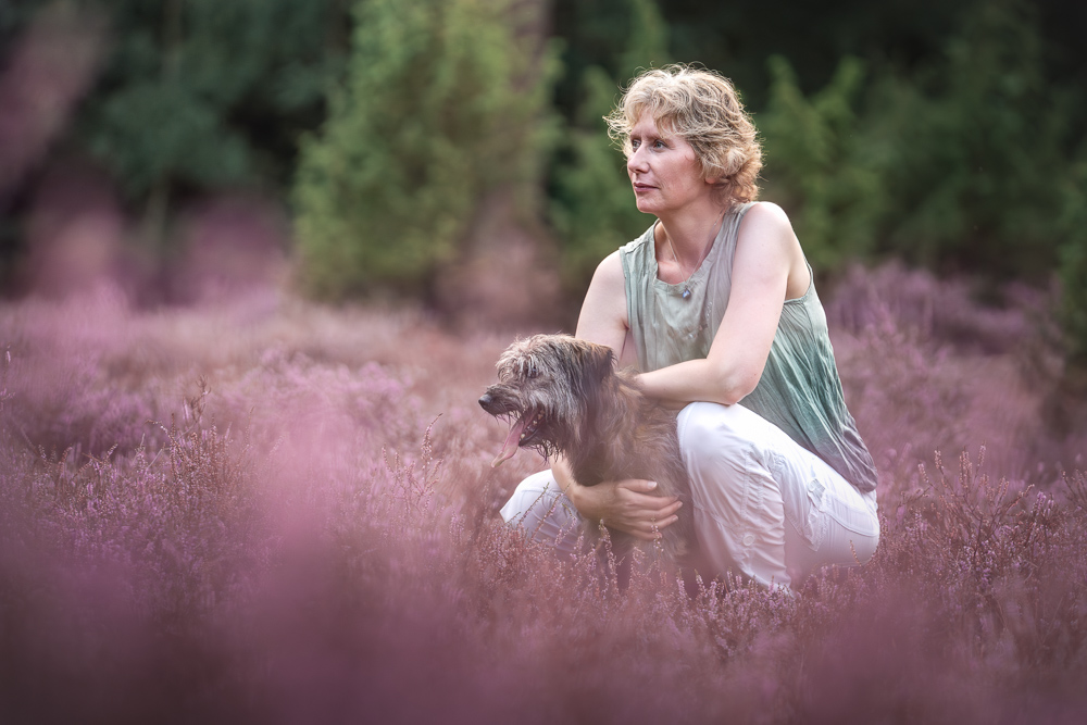 Foto von Lisa Werner Fotografie, Hund und Mensch, Frau sitzt neben einem Hund in lila Heideblüten