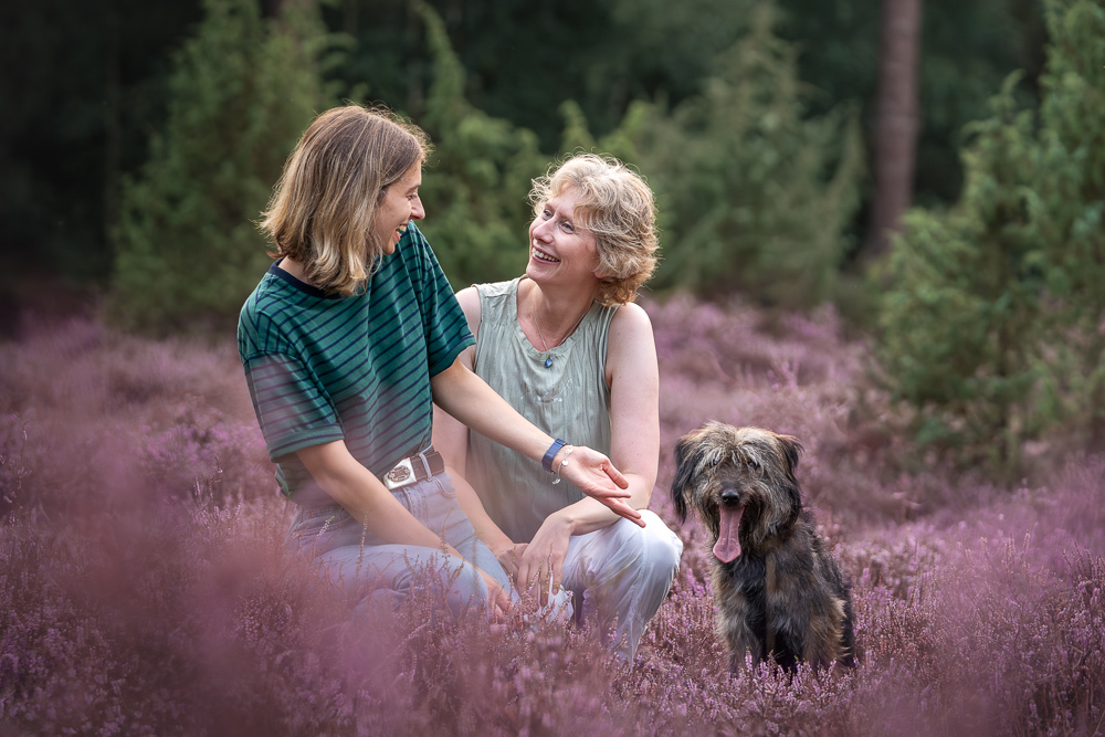 Foto von Lisa Werner Fotografie, Hund und Mensch, Zwei Frauen sitzen neben einem Hund in lila Heideblüten