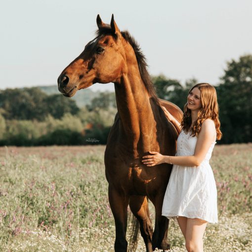 Foto von Lisa Werner Fotografie, Pferd und Mensch, Frau und englisches Vollblut stehen im Blumenfeld